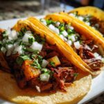 Close-up of three delicious Tacos al pastor filled with marinated pork, topped with diced white onion and cilantro.