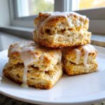 A stack of three flaky, golden brown scones topped with a generous drizzle of white glaze icing.