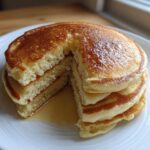 A thick stack of fluffy banana pancakes, cut to show the airy interior, drizzled with syrup.