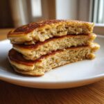 Close-up of a stack of three fluffy banana pancakes cut in half, showing the airy interior texture.