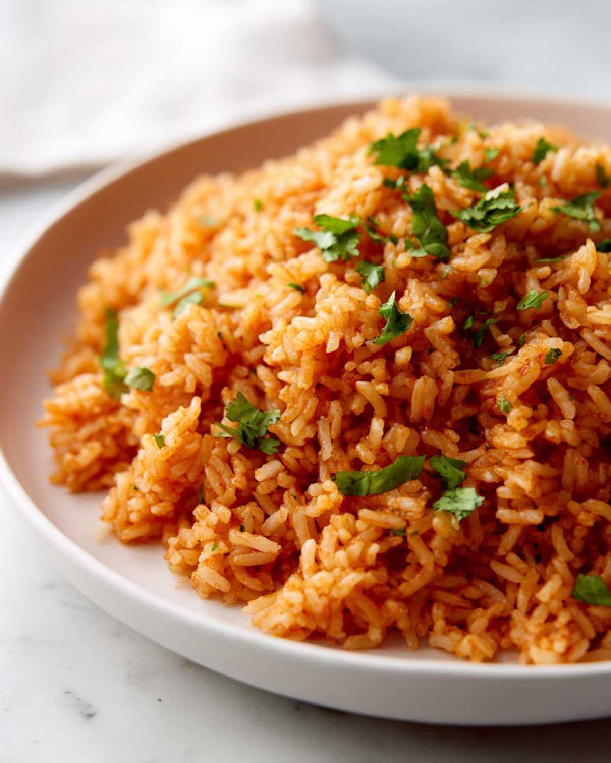 Close-up of fluffy, orange-red Spanish rice served on a white plate and topped with fresh cilantro.