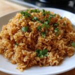 Close-up of a mound of perfectly cooked, seasoned Spanish rice topped with fresh chopped cilantro on a white plate.