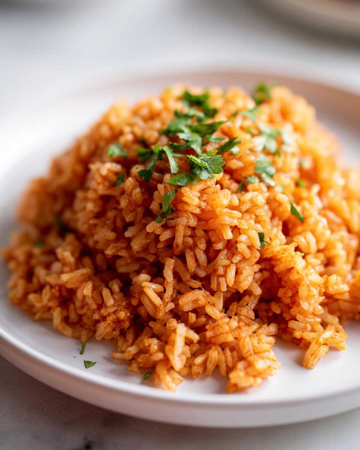 Close-up of a mound of bright orange Spanish rice garnished with fresh chopped parsley on a white plate.