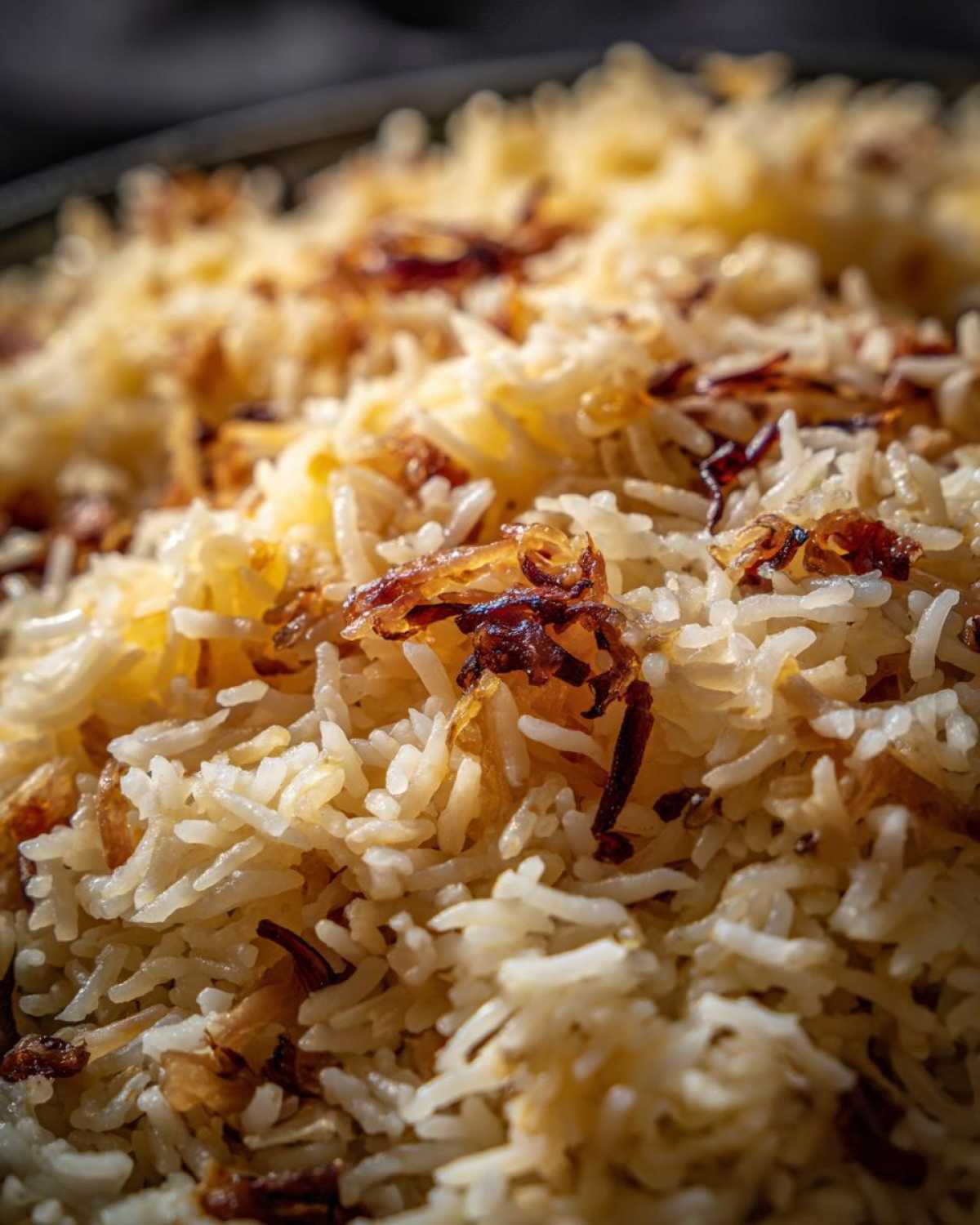 Close-up macro shot of fluffy white rice mixed with melted butter and topped with crispy, caramelized french onion pieces.