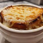 Close-up of a crock of french onion soup topped with a thick layer of melted, browned Gruyère cheese over toasted bread.