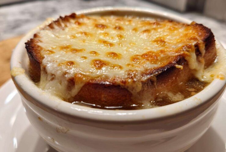 Close-up of a crock of french onion soup topped with a thick layer of melted, browned Gruyère cheese over toasted bread.