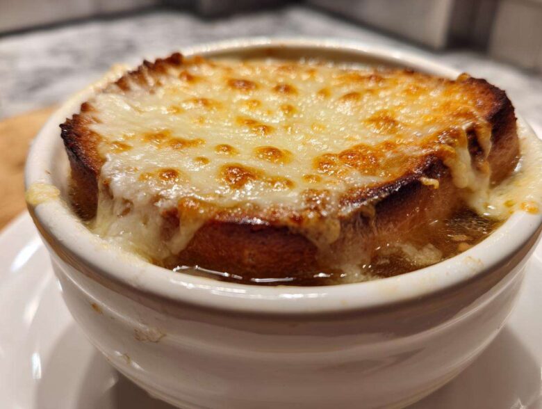 Close-up of a crock of french onion soup topped with a thick layer of melted, browned Gruyère cheese over toasted bread.