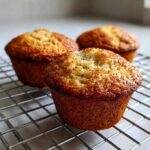 Three golden-brown applesauce muffins cooling on a wire rack, dusted lightly with cinnamon.