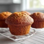 Close-up of golden brown applesauce muffins cooling on a white wire rack indoors.