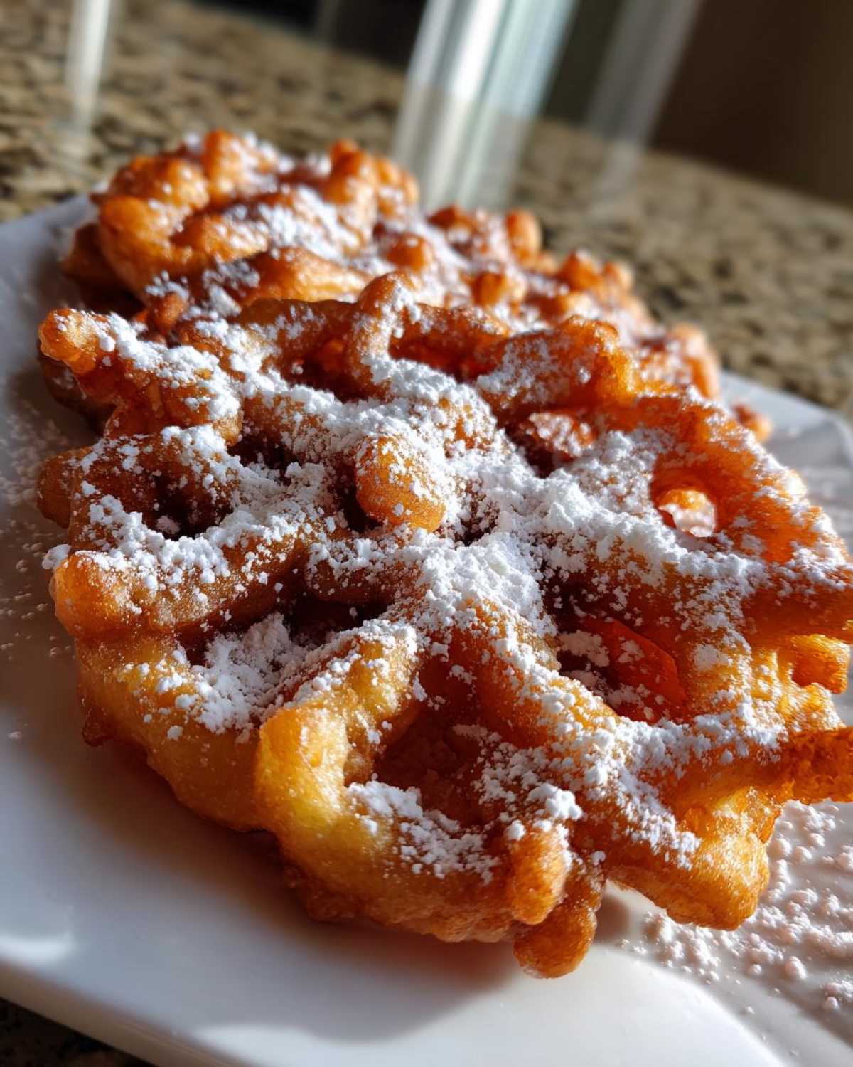 Close-up of golden brown, freshly fried funnel cake recipe dusted heavily with white powdered sugar.