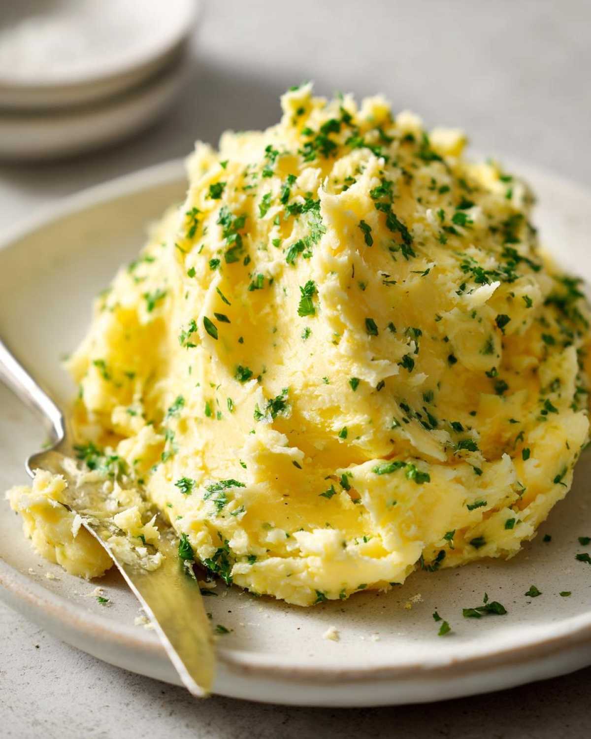 A mound of rich, yellow compound butter mixed with herbs, likely garlic butter, served on a plate.
