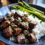 Close-up of a Garlic Butter Steak Bowl featuring juicy steak bites coated in garlic butter sauce over white rice and served with bright green asparagus.