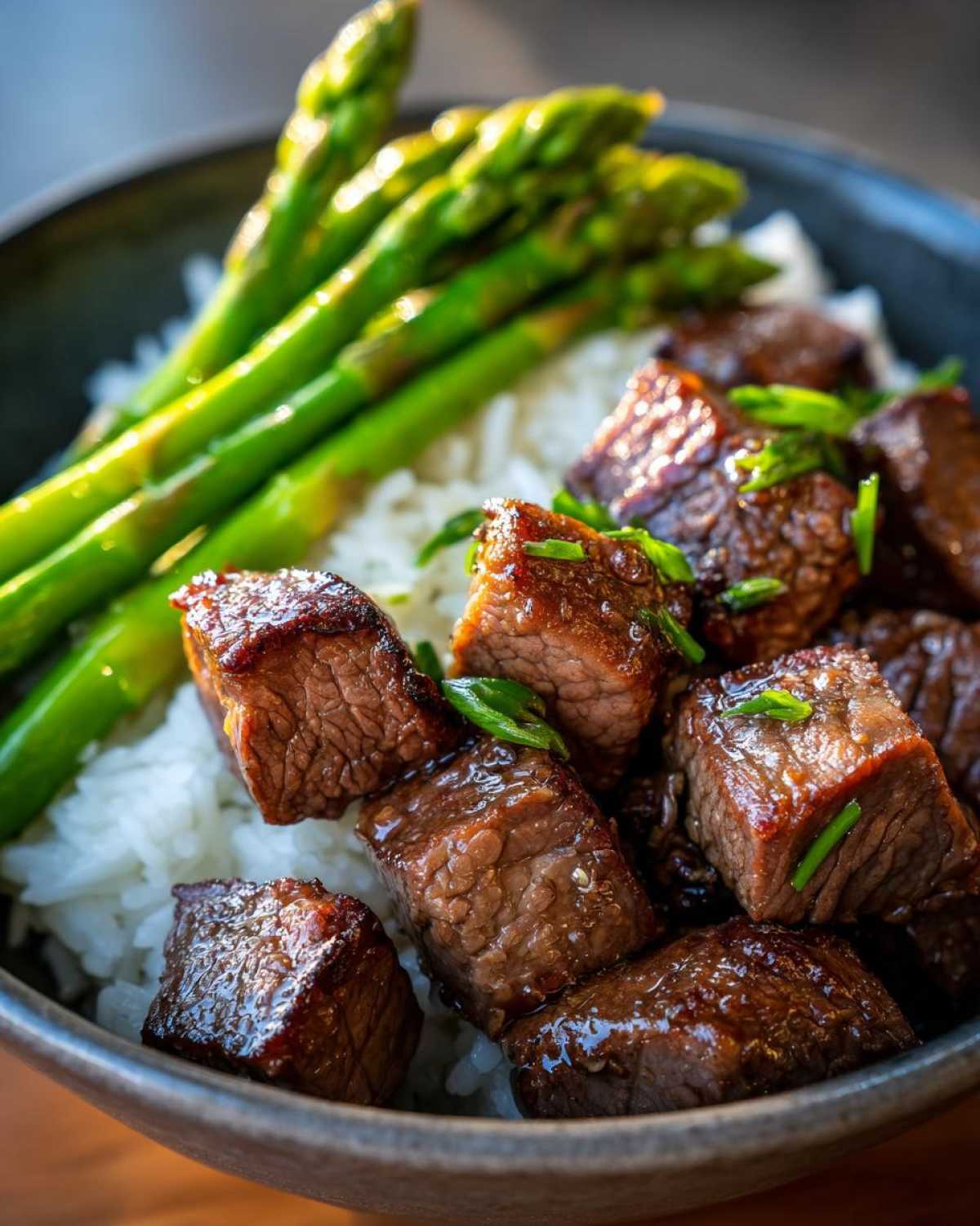Close-up of a Garlic Butter Steak Bowl featuring juicy steak cubes, white rice, and bright green asparagus spears.