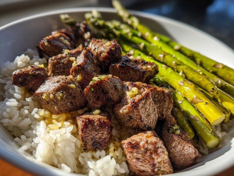 Close-up of a Garlic Butter Steak Bowl Weeknight Dinner featuring steak bites over white rice with bright green asparagus.