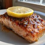 A perfectly cooked piece of baked salmon recipe fillet, glazed with a shiny sauce and topped with a lemon slice.