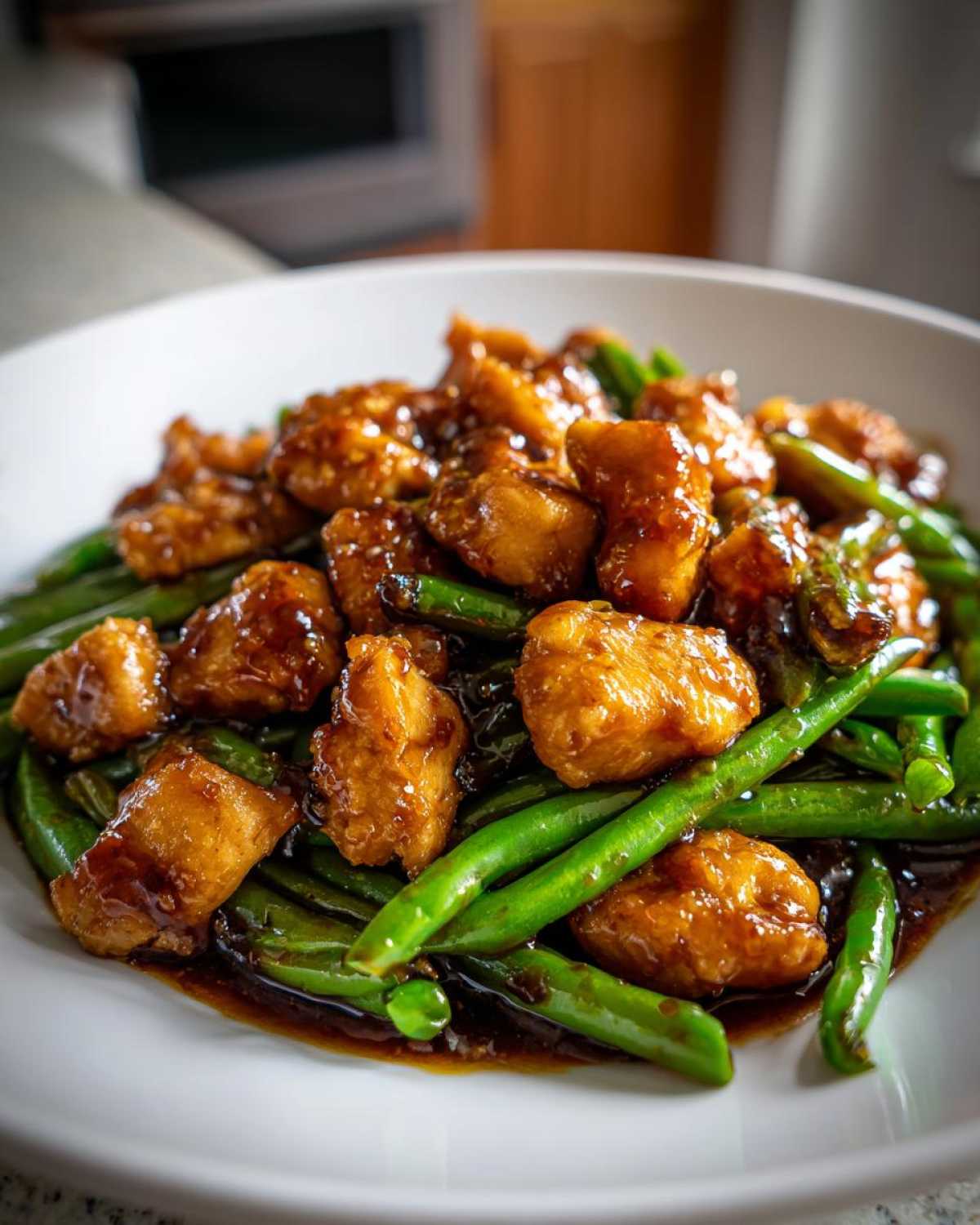 Close-up of glazed chicken pieces served over bright green beans, a delicious chicken and green beans dinner.