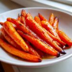 A close-up shot of perfectly caramelized and glazed roasted carrots served in a white bowl.