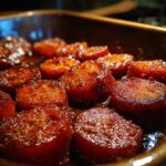 Close-up of thick-cut, glazed southern candied yams simmering in a rich, brown sugar syrup in a baking dish.