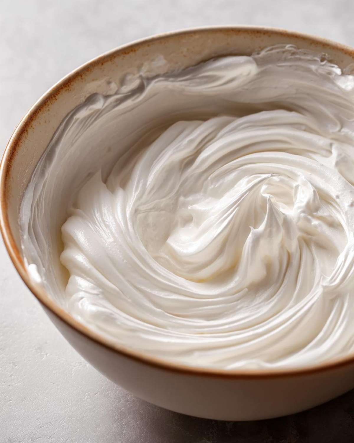 Close-up of thick, glossy white royal icing recipe mixture swirled in a ceramic bowl.