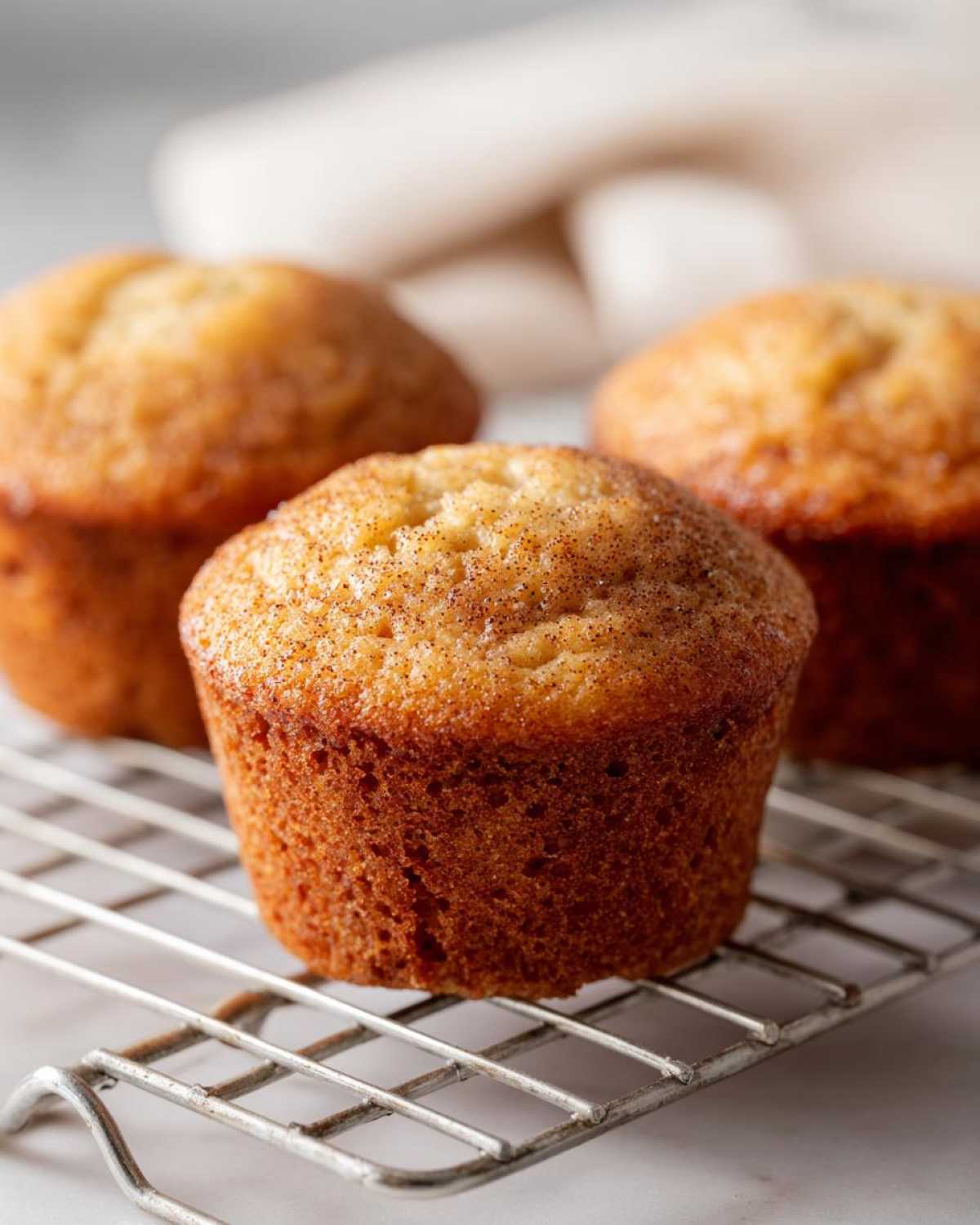 Three golden brown applesauce muffins cooling on a wire rack, topped with cinnamon sugar.