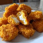 A pile of crispy, golden homemade chicken nuggets on a white plate, one nugget broken open showing the white chicken interior.