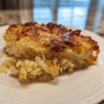 A close-up of a golden-brown, cheesy slice of funeral potatoes recipe served on a white plate.