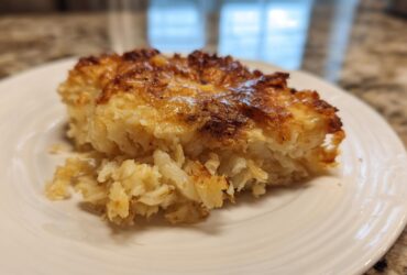 A close-up of a golden-brown, cheesy slice of funeral potatoes recipe served on a white plate.