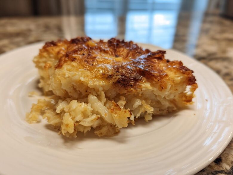 A close-up of a golden-brown, cheesy slice of funeral potatoes recipe served on a white plate.