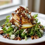 Close-up of a vibrant pear salad featuring sliced pears, arugula, blue cheese crumbles, walnuts, and balsamic glaze.