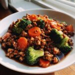A close-up of Ground Chicken Teriyaki Stir Fry Weeknight Delight with ground chicken, bright green broccoli florets, and sliced carrots in a savory sauce.