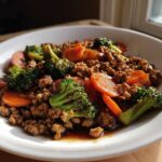 A close-up of Ground Chicken Teriyaki Stir Fry with bright green broccoli florets and sliced carrots in a white bowl.