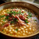 Close-up of a bowl of hearty navy bean soup topped with shredded ham and fresh parsley.
