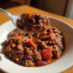 A spoonful of hearty high protein chili, rich with ground meat and kidney beans, lifted from a bowl.