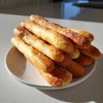 A stack of golden brown, buttery Homemade Breadsticks Inspired by Olive Garden sprinkled with coarse salt.