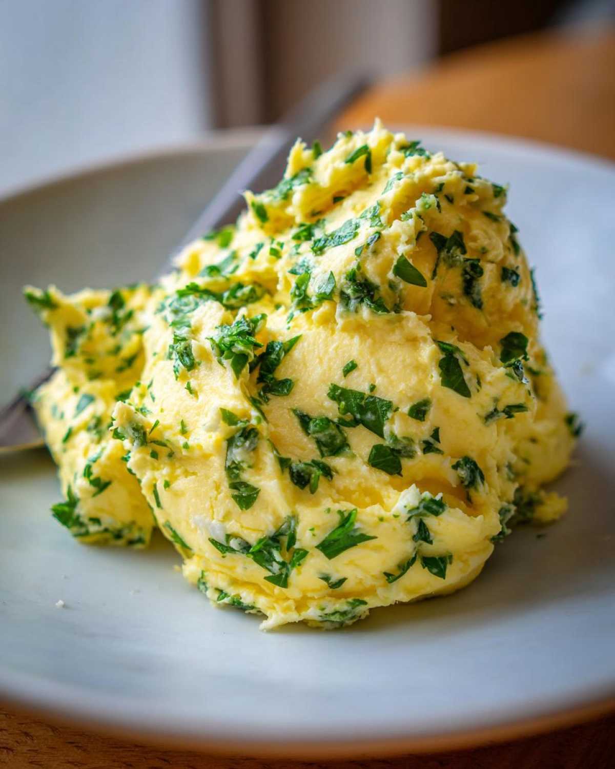 A generous dollop of bright yellow homemade garlic butter mixed with chopped green parsley served on a light plate.