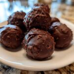 Close-up of several homemade Oreo Cake Balls coated in rich dark chocolate, piled on a small white plate.