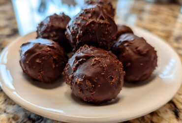 Close-up of several homemade Oreo Cake Balls coated in rich dark chocolate, piled on a small white plate.