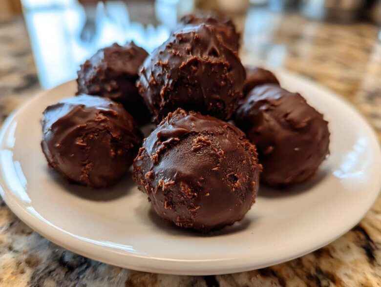 Close-up of several homemade Oreo Cake Balls coated in rich dark chocolate, piled on a small white plate.