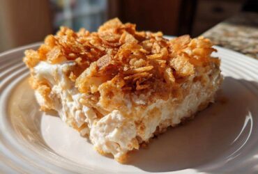 A square serving of creamy hot chicken salad bake topped with a thick layer of golden, crunchy cornflakes.