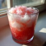 Close-up of a frosty glass filled with icy, layered Irresistible Strawberry Piña Colada Punch.