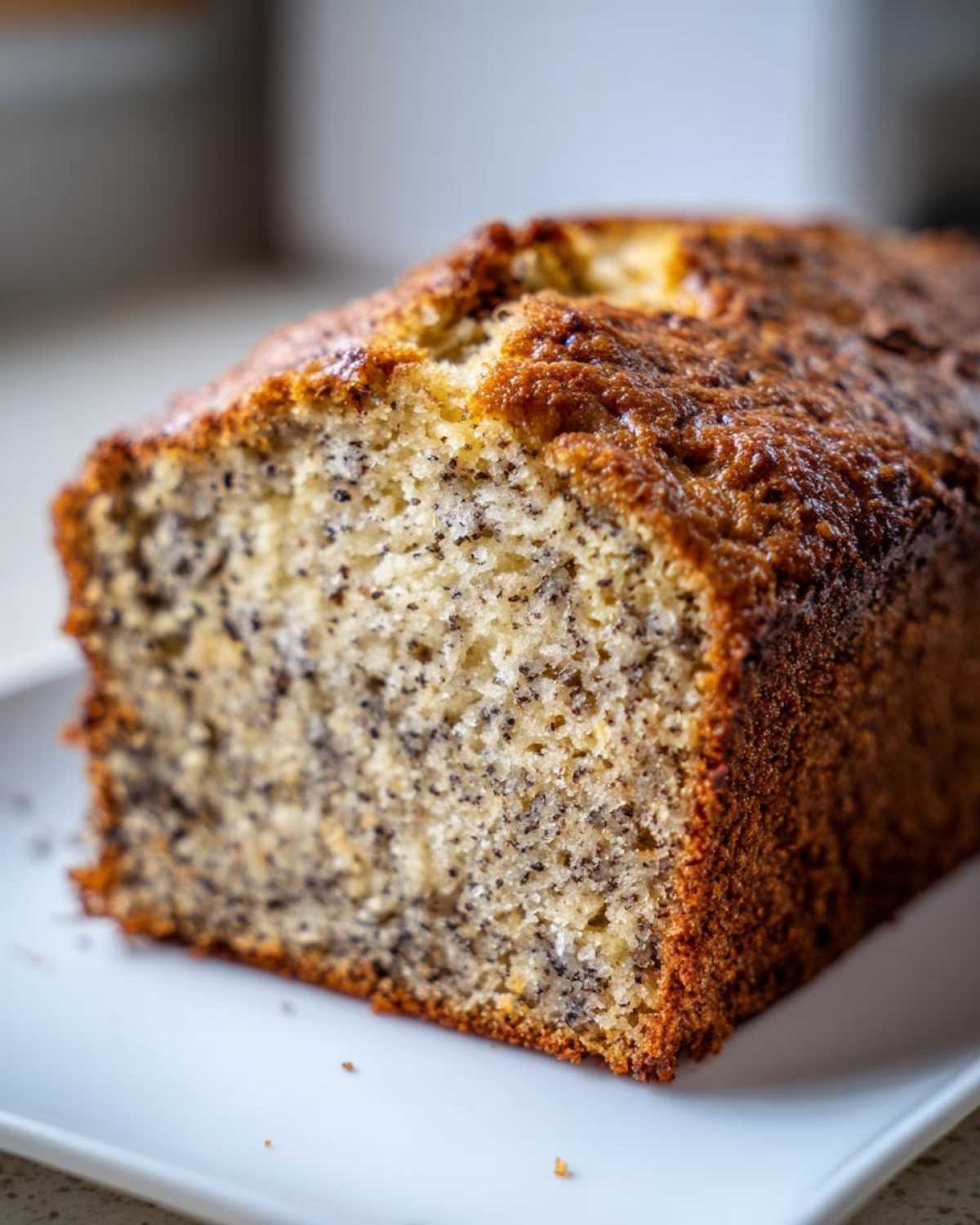 Close-up of a slice of incredibly moist banana bread showing a tender crumb speckled with dark banana bits.