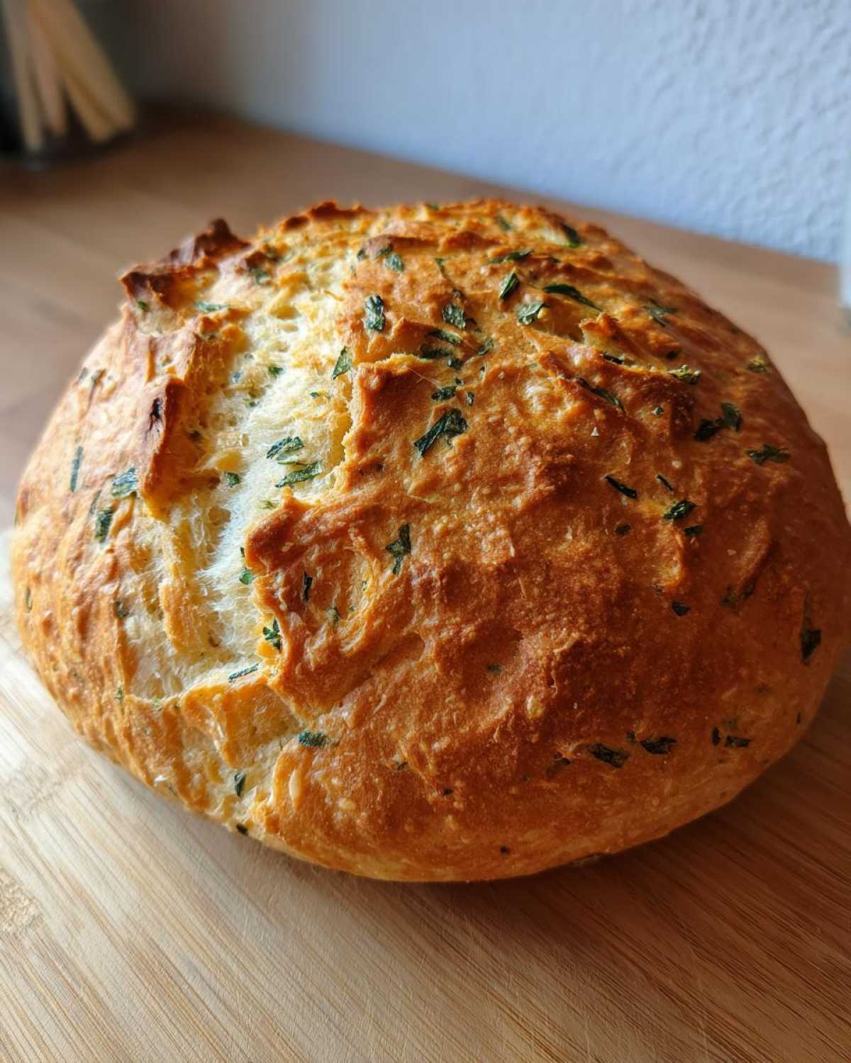 A golden-brown, rustic loaf of Italian herb and cheese bread with visible herbs baked into the crust.