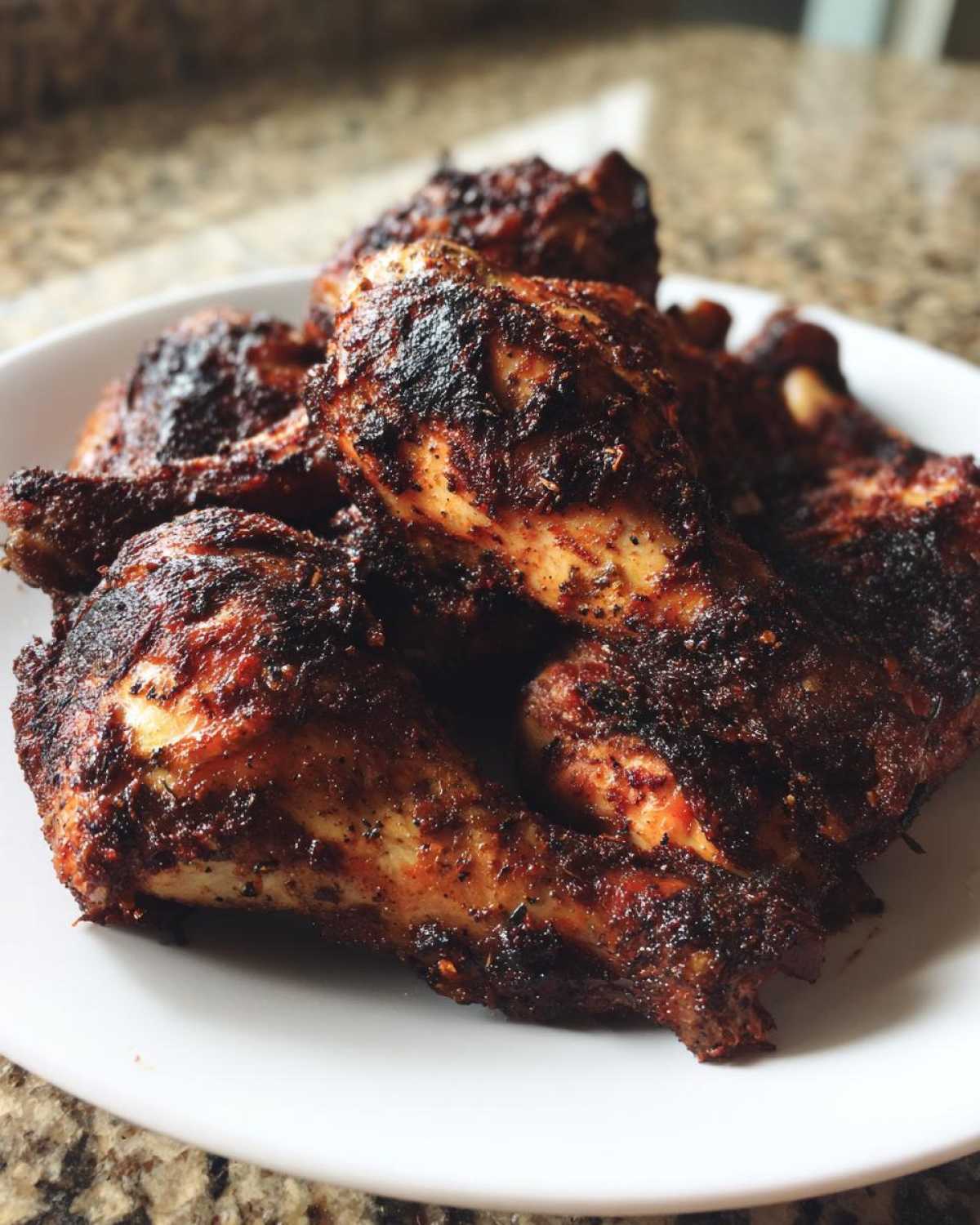 A pile of perfectly cooked Jamaican jerk chicken pieces with a dark, spicy crust served on a white plate.