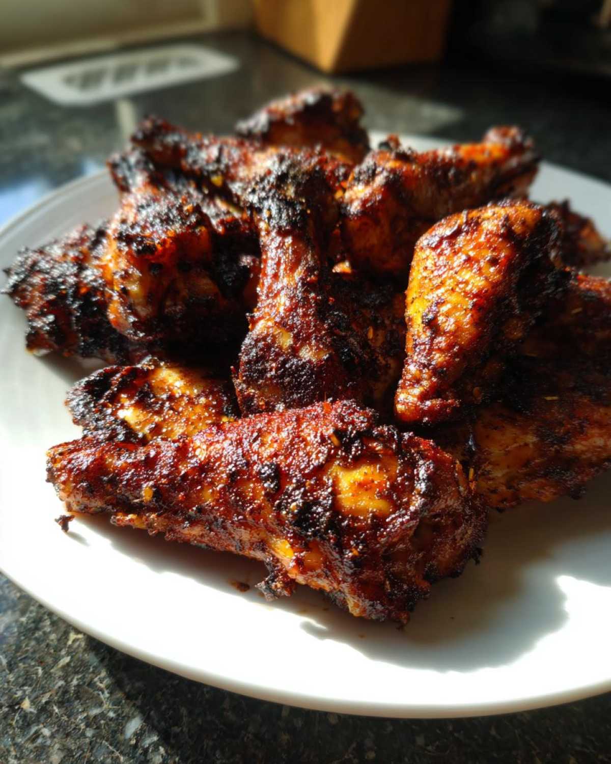 Close-up of a white plate piled high with perfectly cooked Jamaican jerk chicken wings, showing a rich, dark spice crust.