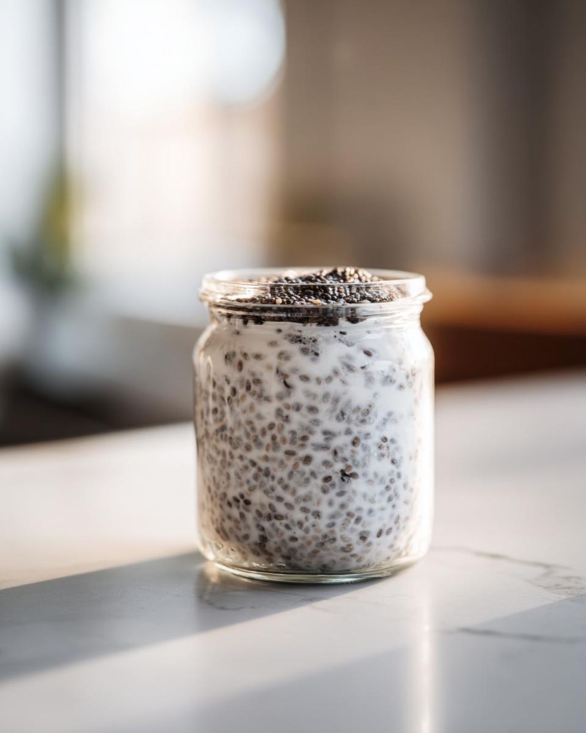 A glass jar filled with creamy, prepared chia seed pudding, topped with extra chia seeds.