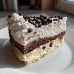 A decadent slice of layered ice cream cake featuring vanilla, chocolate, and whipped cream topping with chocolate chips.