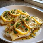 Two fillets of white fish served as a Seafood Dish, topped with glistening lemon slices and fresh parsley.