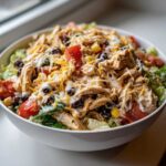 Close-up of a hearty southwest salad topped with shredded chicken, black beans, corn, tomatoes, cheese, and creamy dressing.