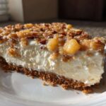 A close-up shot of a thick slice of million dollar pie featuring a graham cracker crust, creamy white filling, and a pecan and fruit topping.