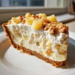 A close-up slice of rich million dollar pie featuring a graham cracker crust, creamy filling, and topped with pineapple chunks and walnuts.